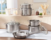 Topfset Brillant 6-tlg. aus Edelstahl, bestehend aus mehreren Töpfen und einer Pfanne mit Glasdeckeln, auf einem Tisch in einer hellen Küche präsentiert. Perspektive: seitlich.