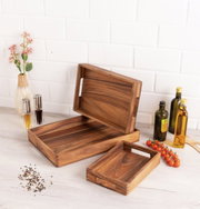 Holztablett-Set in verschiedenen Größen, präsentiert auf einem Tisch mit Gewürzen und Ölen, aus seitlicher Perspektive.