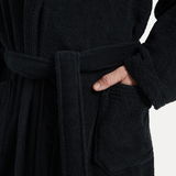 Nahaufnahme eines schwarzen Bademantels mit Schalkragen, Gürtel und Tasche, Hand in der Tasche.