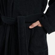 Nahaufnahme eines schwarzen Bademantels mit Schalkragen, Gürtel und Tasche, Hand in der Tasche.