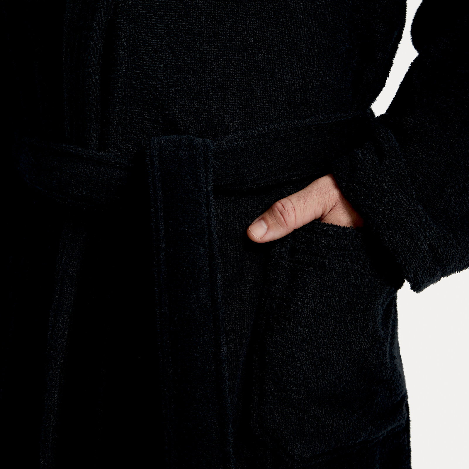 Nahaufnahme eines schwarzen Bademantels mit Schalkragen, Gürtel und Tasche, Hand in der Tasche.