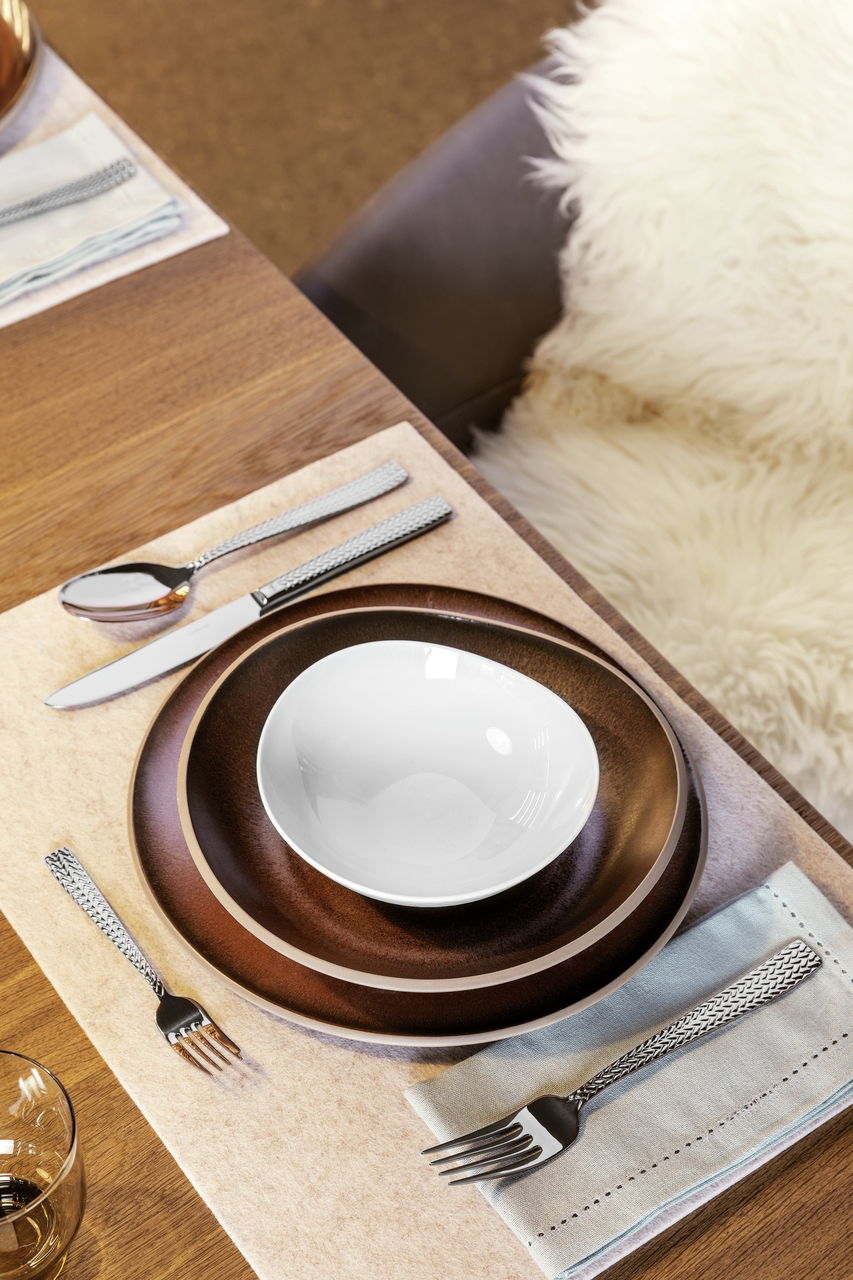Elegantes Besteckset Cortina 30-tlg. auf einem gedeckten Tisch mit braunen Tellern und weißer Schale, aus der Vogelperspektive.