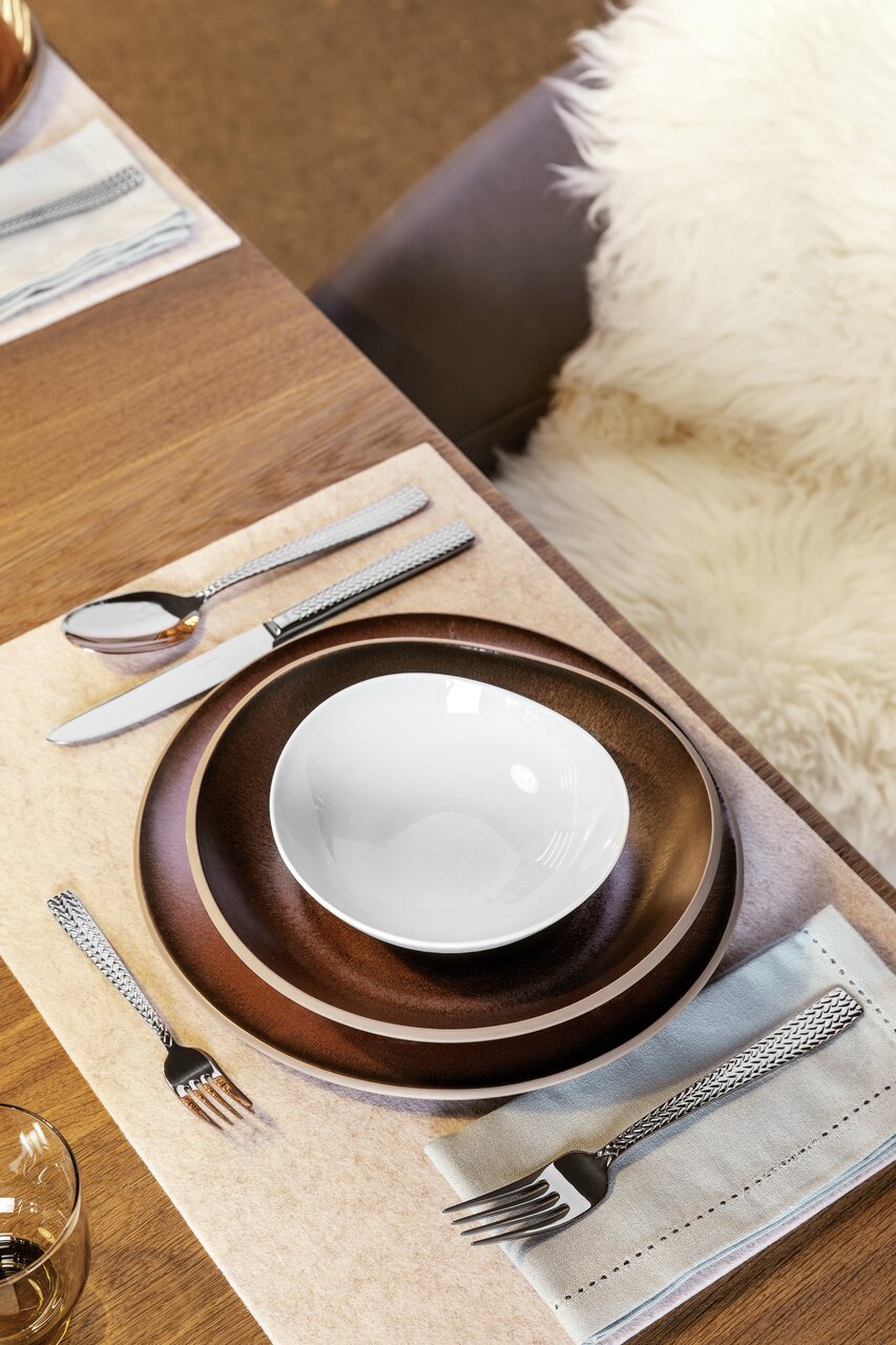 Elegante bestekset Cortina (30-delig) op een gedekte tafel met bruine borden en een witte schaal, gezien vanuit vogelperspectief.