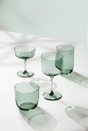 Set aus vier grünen Gläsern, bestehend aus zwei Longdrinkgläsern und zwei Weingläsern, auf einer weißen Oberfläche aus der Vogelperspektive fotografiert.
