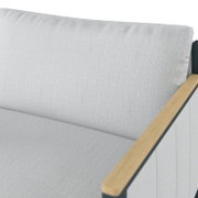 Detailfoto van een loungebank met een lichte stoffen bekleding en een houten armleuning aan de rechterkant.