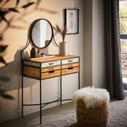 Schminktisch aus Holz und Metall mit rundem Spiegel, dekoriert mit einer Vase und Kosmetikflaschen, seitliche Perspektive.