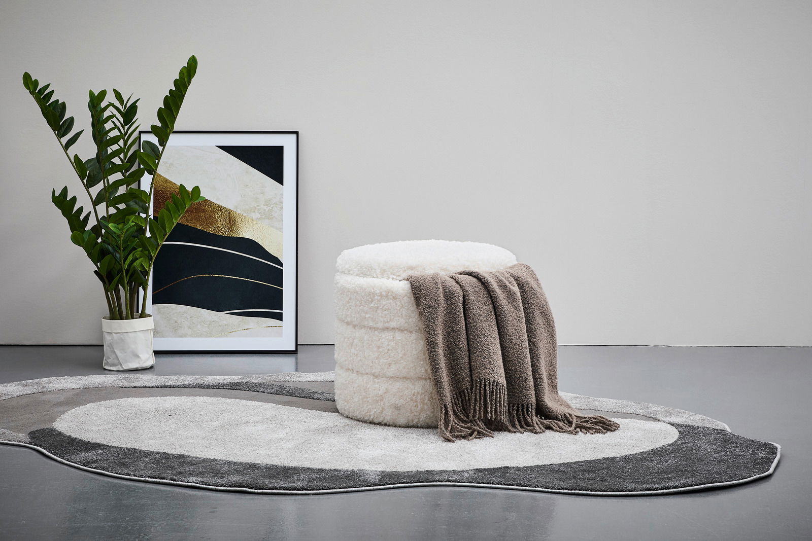 Hocker mit Stauraum in cremefarbener Textur, dekoriert mit einer braunen Decke, auf einem gemusterten Teppich, seitliche Perspektive.