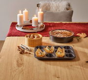 Muffin-Blech mit 12 Vertiefungen, teilweise mit Muffins gefüllt, auf einem Tisch aus Holz, aus der Vogelperspektive fotografiert.