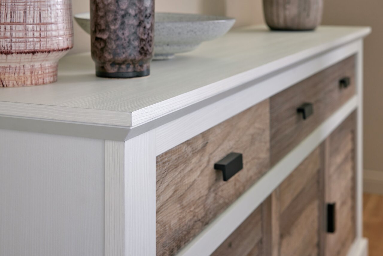 Close-up van een modern dressoir met een wit frame en houten fronten, versierd met vazen en een schaal, gezien vanuit de zijkant.