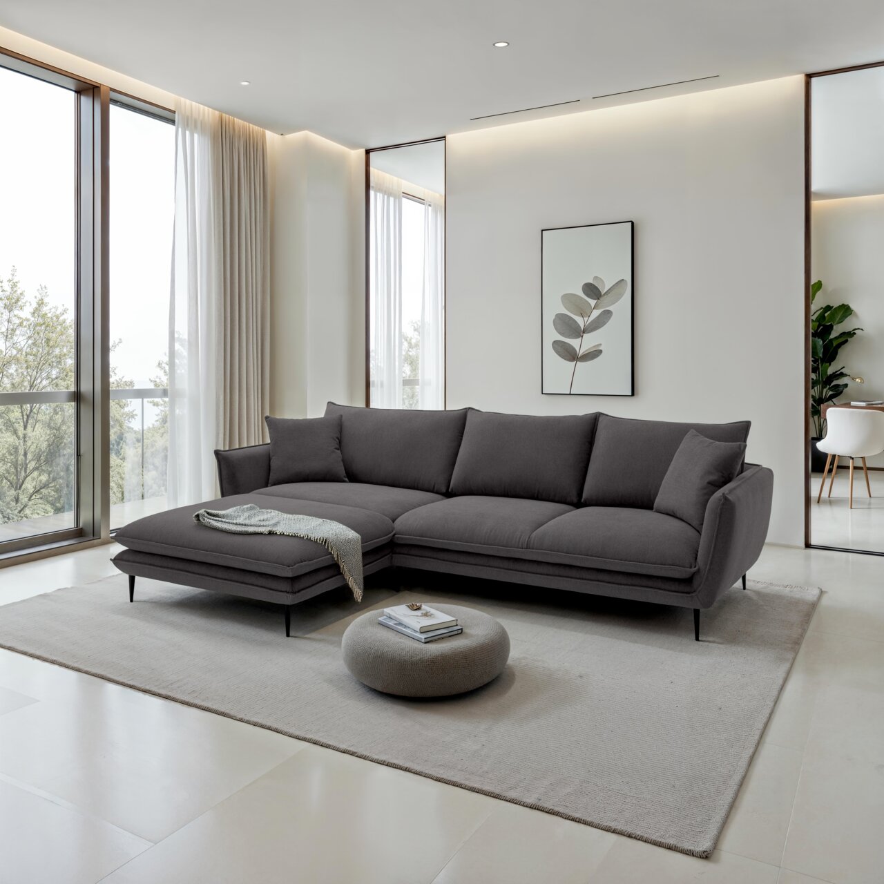 Moderne donkergrijze hoekbank met een poef aan de linkerkant en zwarte metalen poten in een lichte woonkamer, licht schuin perspectief van linksvoor.