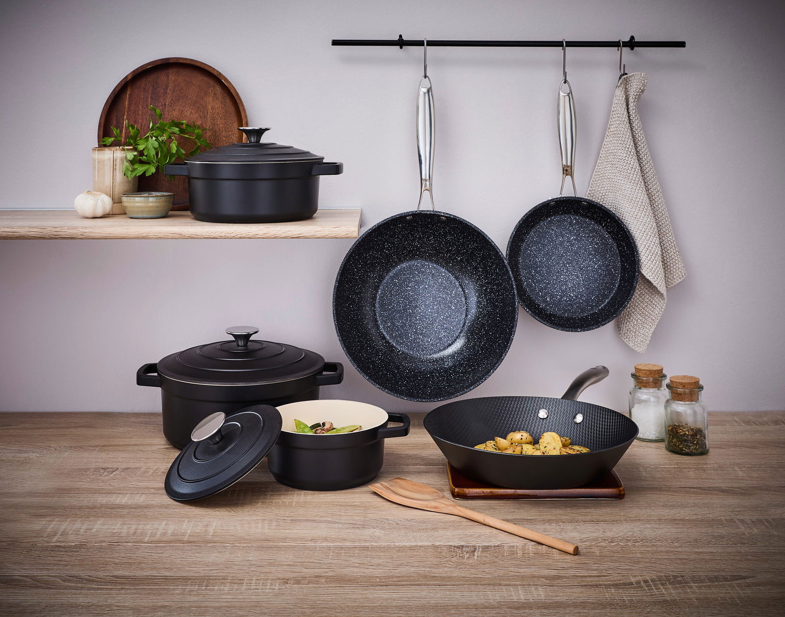 Wokpfanne 28cm, schwarz, in einer modernen Küchenszene, von vorne betrachtet, mit weiteren Kochutensilien und Gewürzen im Hintergrund.