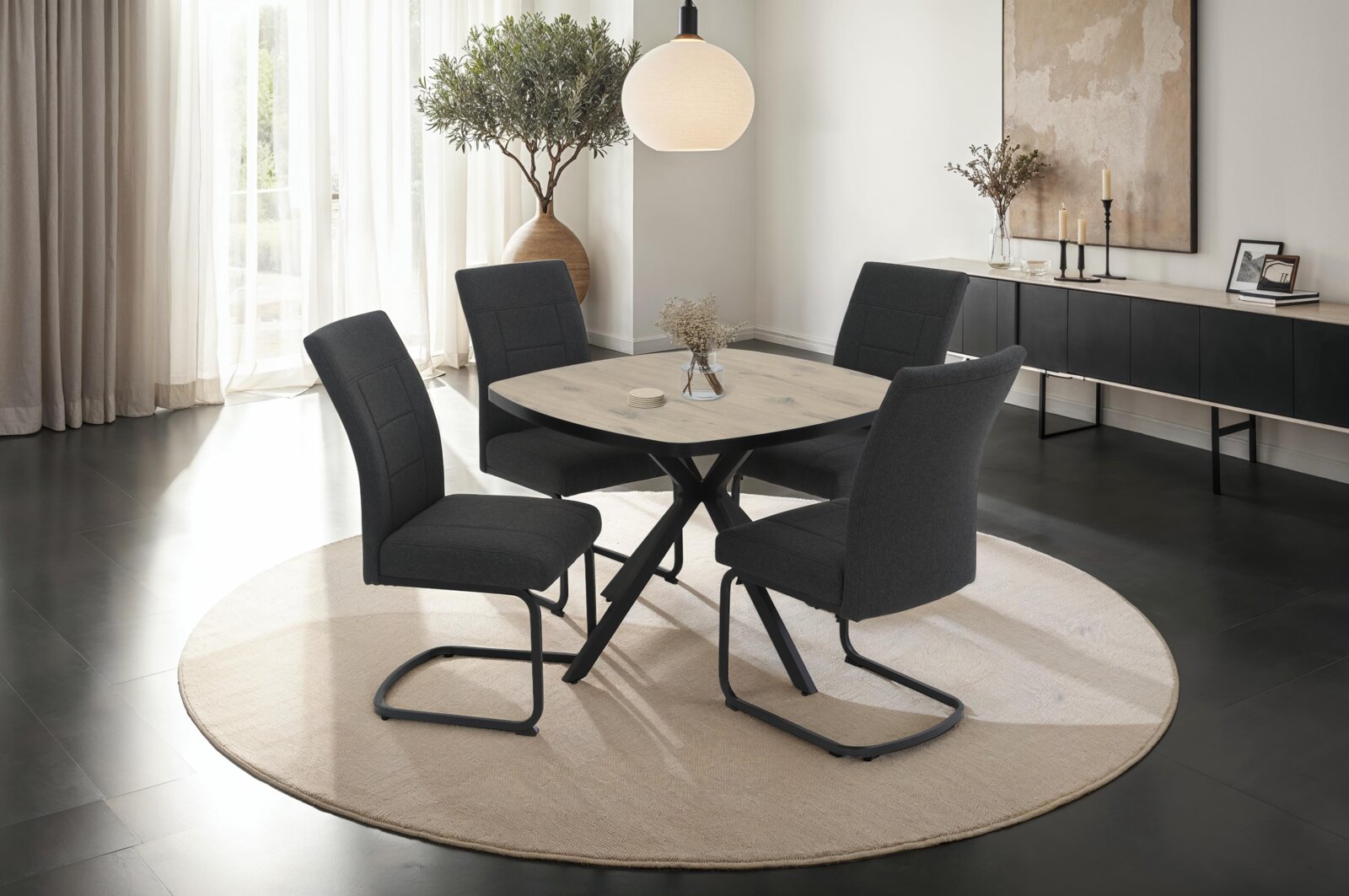 Z2 Esstisch ROTTERDAM Moderner Esstisch mit runder Holzplatte und schwarzen Metallbeinen, umgeben von vier dunkel gepolsterten Stühlen auf einem hellen Teppich. Perspektive: seitlich.