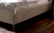 Nahaufnahme eines Polsterbetts in Beige mit Holzfüßen, seitliche Perspektive