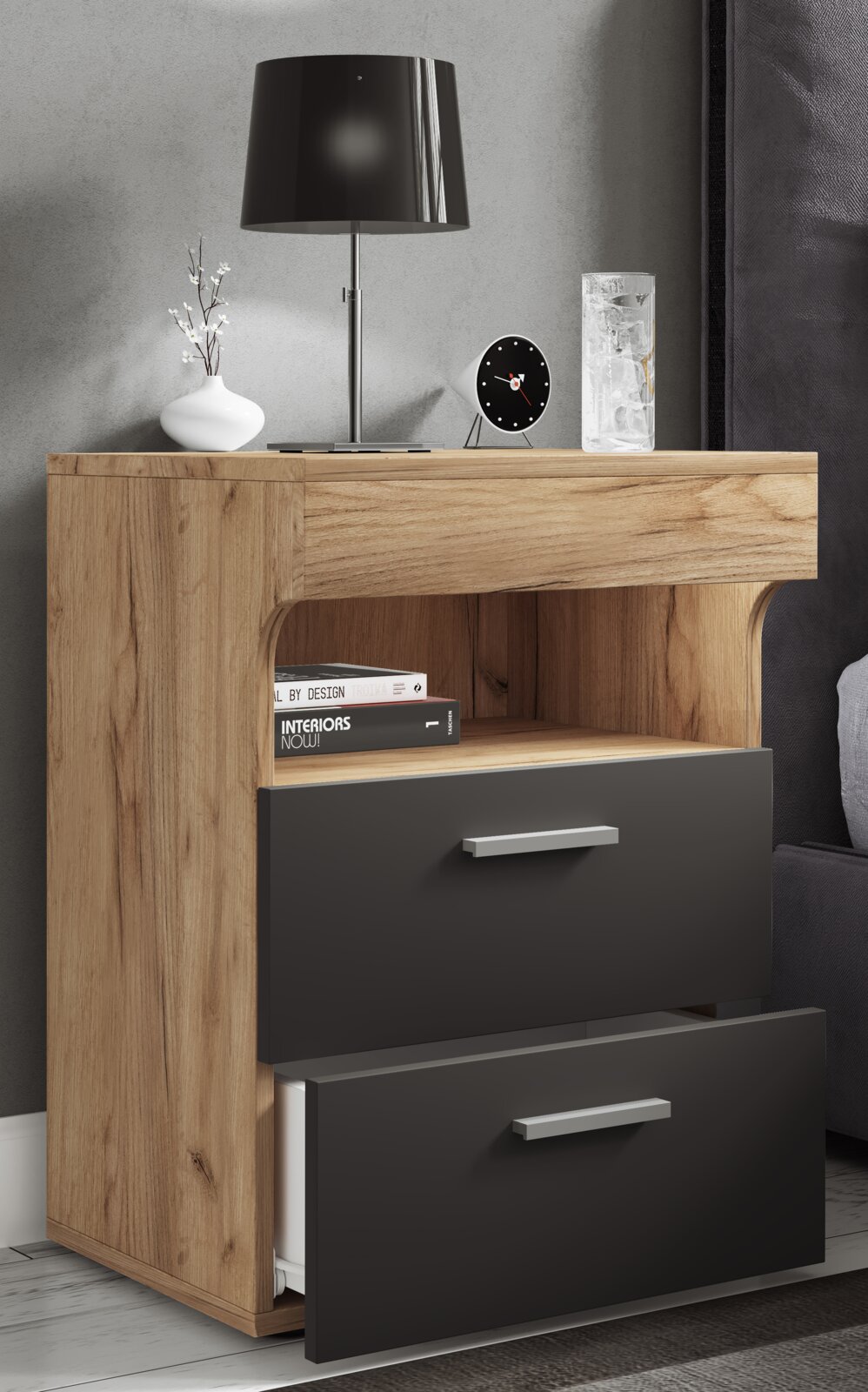 Modernes Nachtkästchen/Beistellschrank in Holzoptik mit zwei anthrazitfarbenen Schubladen und offenem Fach, dekoriert mit Tischlampe, Vase, Uhr und Glas; Perspektive: frontale Ansicht leicht von rechts.