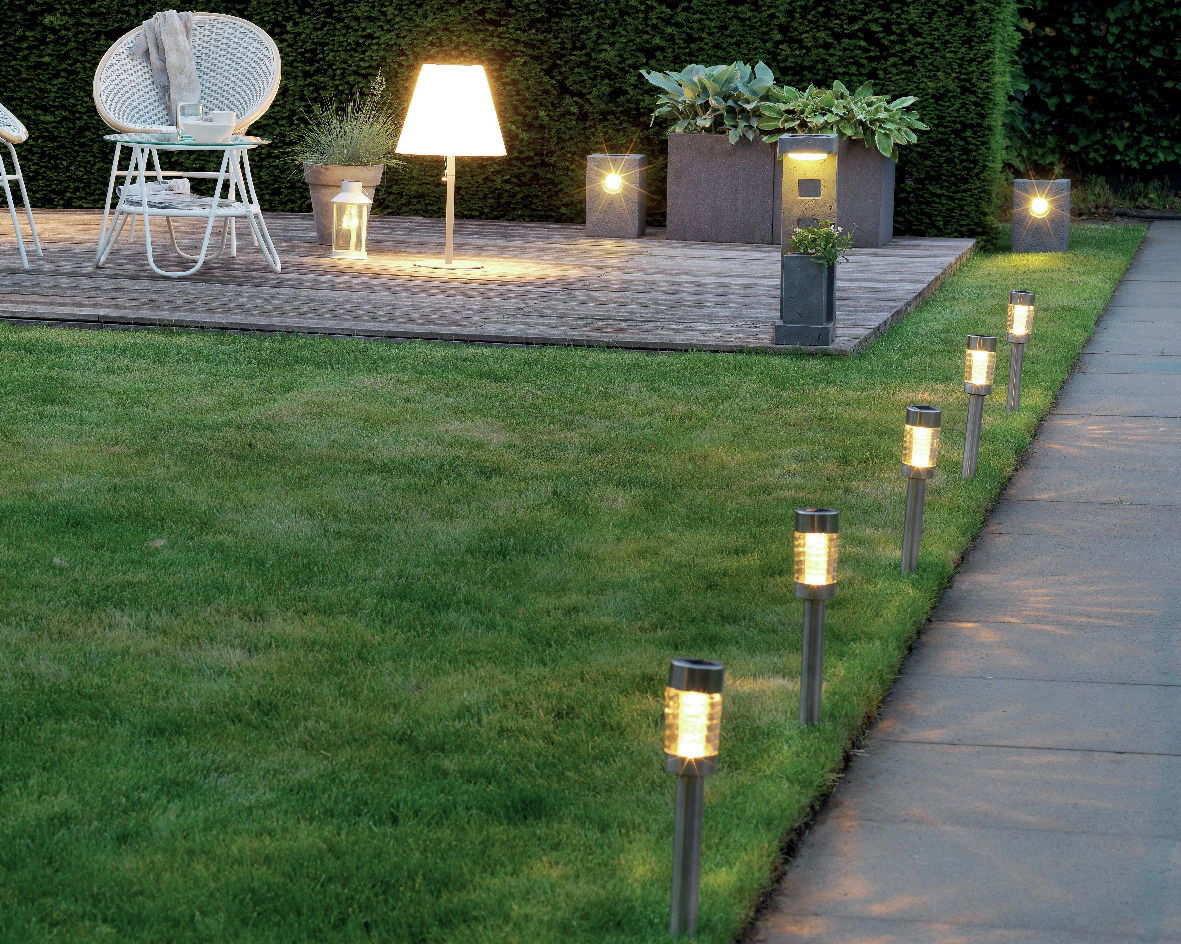Garten mit mehreren Solar Stabbeleuchtungen aus Edelstahl, die entlang eines Weges aufgestellt sind. Perspektive von der Seite, die die Beleuchtung und den Gartenbereich zeigt.