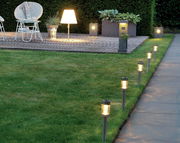 Garten mit mehreren Solar Stabbeleuchtungen aus Edelstahl, die entlang eines Weges aufgestellt sind. Perspektive von der Seite, die die Beleuchtung und den Gartenbereich zeigt.