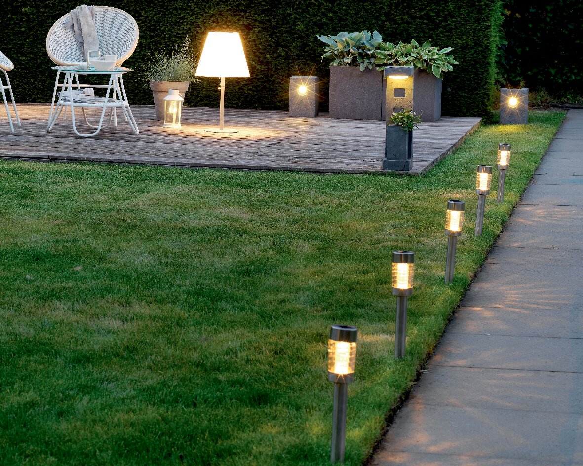 Garten mit mehreren Solar Stabbeleuchtungen aus Edelstahl, die entlang eines Weges aufgestellt sind. Perspektive von der Seite, die die Beleuchtung und den Gartenbereich zeigt.