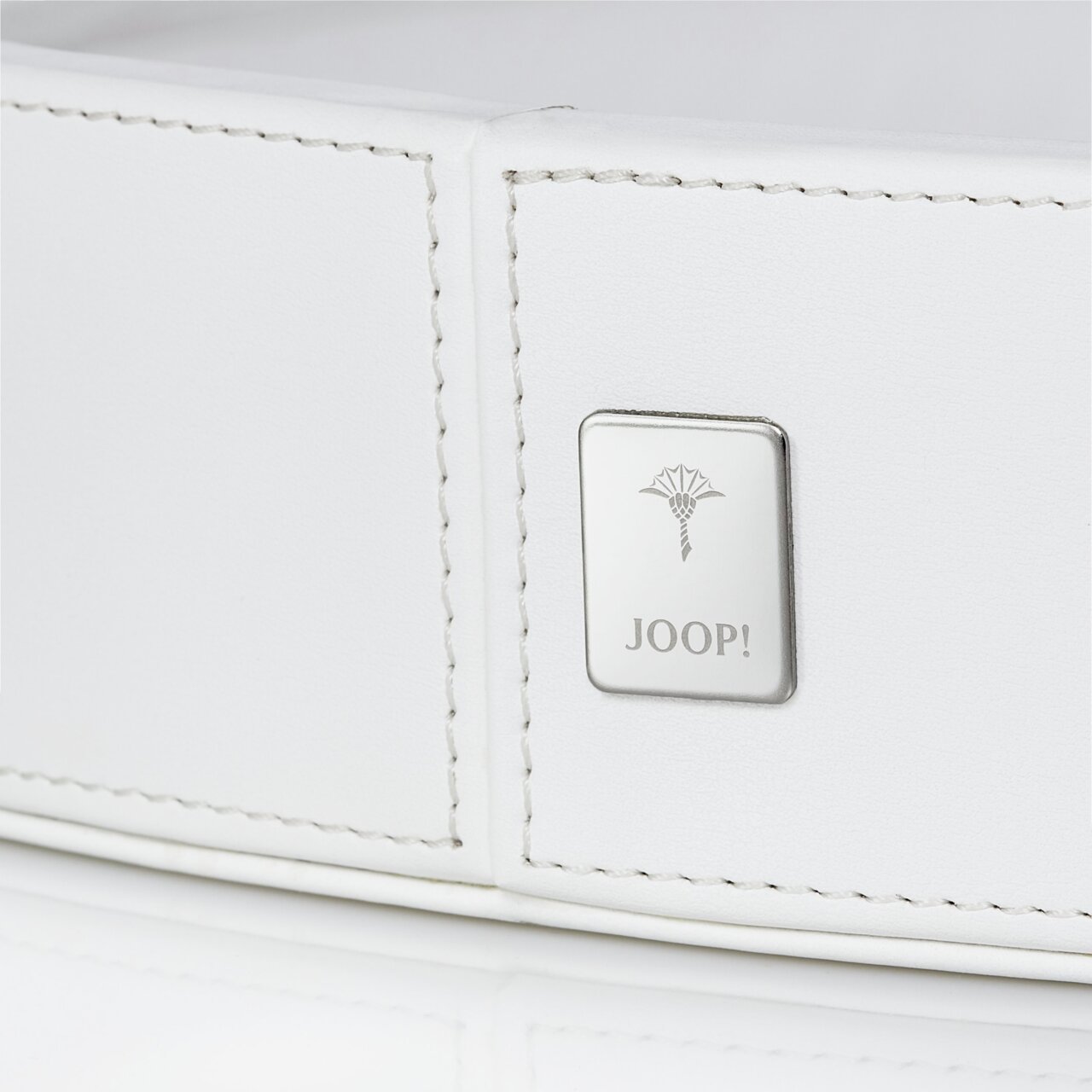 Nahaufnahme eines großen, weißen, runden Tabletts mit einem silbernen Joop!-Logo auf der Seite.