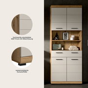 Hoher Badschrank in Holzoptik mit weißen MDF-Fronten und schwarzen Griffen, mittig offene Ablage mit Deko und Handtüchern; Frontansicht.
