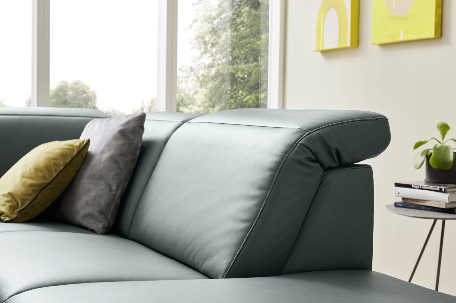 Nahaufnahme eines modernen Ecksofas Musterring MR 1320 in einem hellen Raum mit großen Fenstern, dekoriert mit Kissen in verschiedenen Farben, seitliche Perspektive.