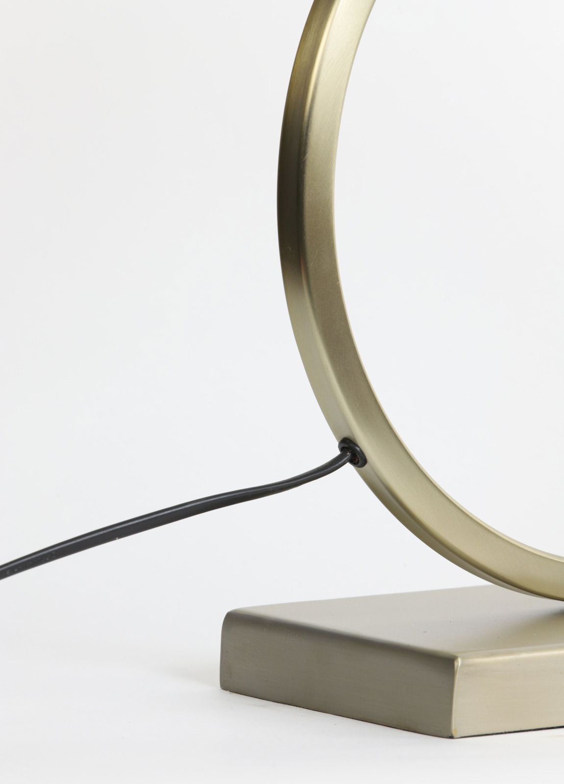 Nahaufnahme eines modernen, goldfarbenen Lampenfußes mit rundem Design und schwarzem Kabel, seitliche Perspektive.