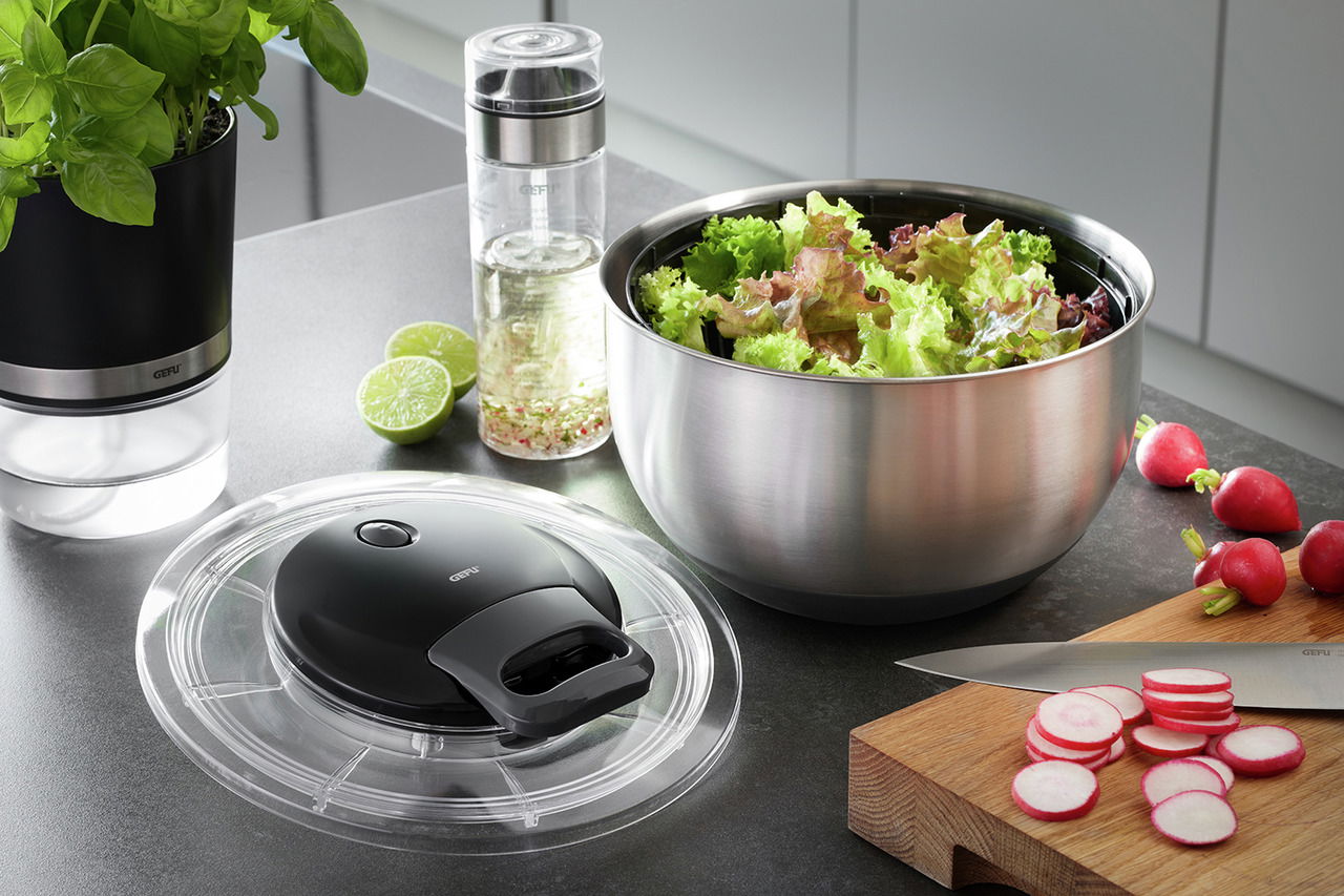 Salatschleuder PULLIT aus Edelstahl mit frischem Salat, abnehmbarem Deckel im Vordergrund, seitliche Perspektive.