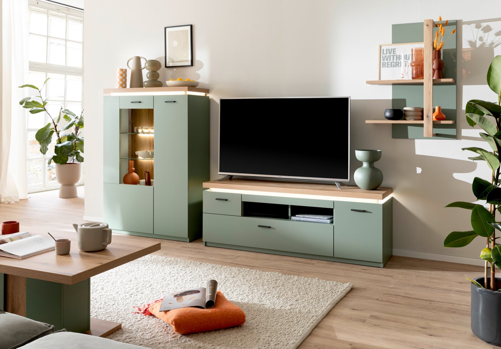 Z2 Highboard MONITZ Modernes Wohnzimmer-Setup mit mintgrüner TV-Wohnwand und passendem Vitrinenschrank in Holzoptik, Fernseher auf Lowboard und Wandregal mit Deko, aufgenommen in frontaler Perspektive auf die Möbel.