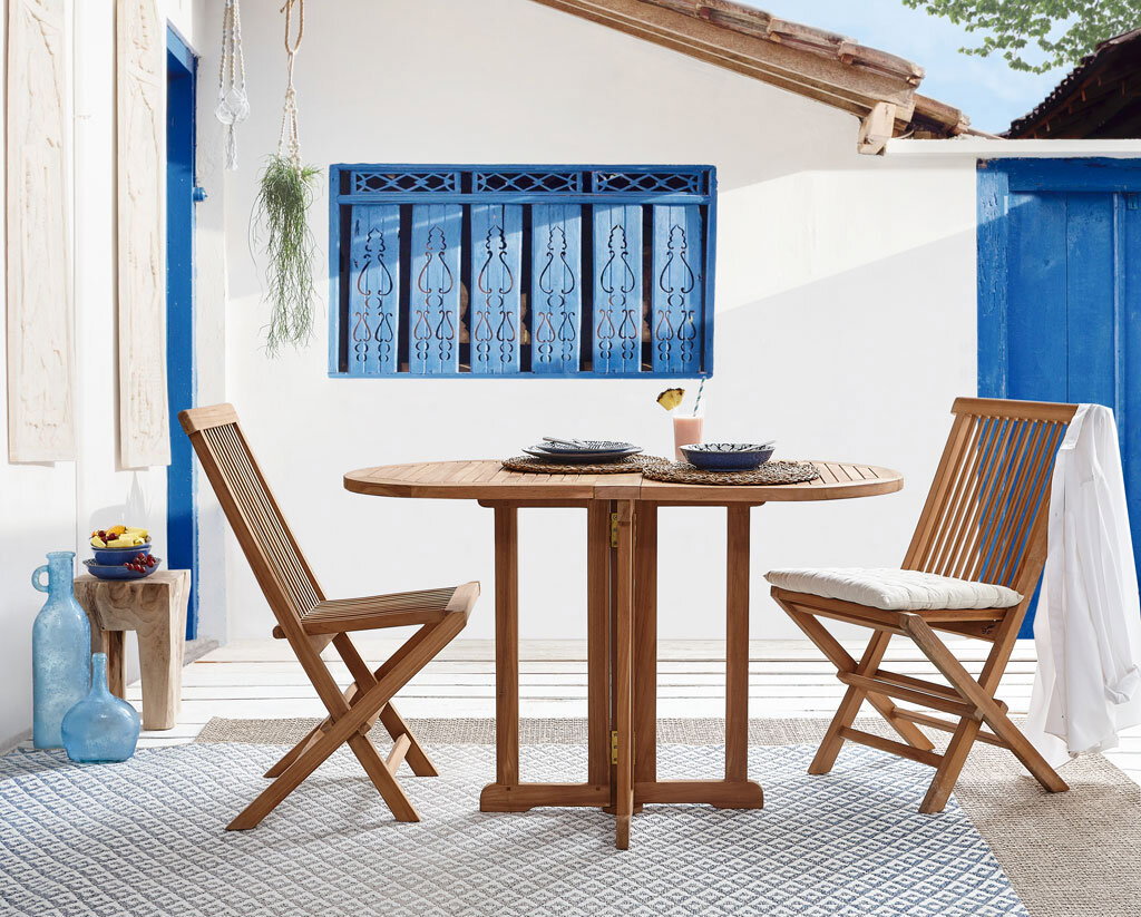 Gartentisch aus Holz mit zwei passenden Stühlen, seitliche Perspektive, auf einer Terrasse mit blauen Akzenten.