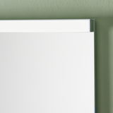 Nahaufnahme eines modernen Badezimmerspiegels mit schmalem Rahmen, montiert an einer grünen Wand.