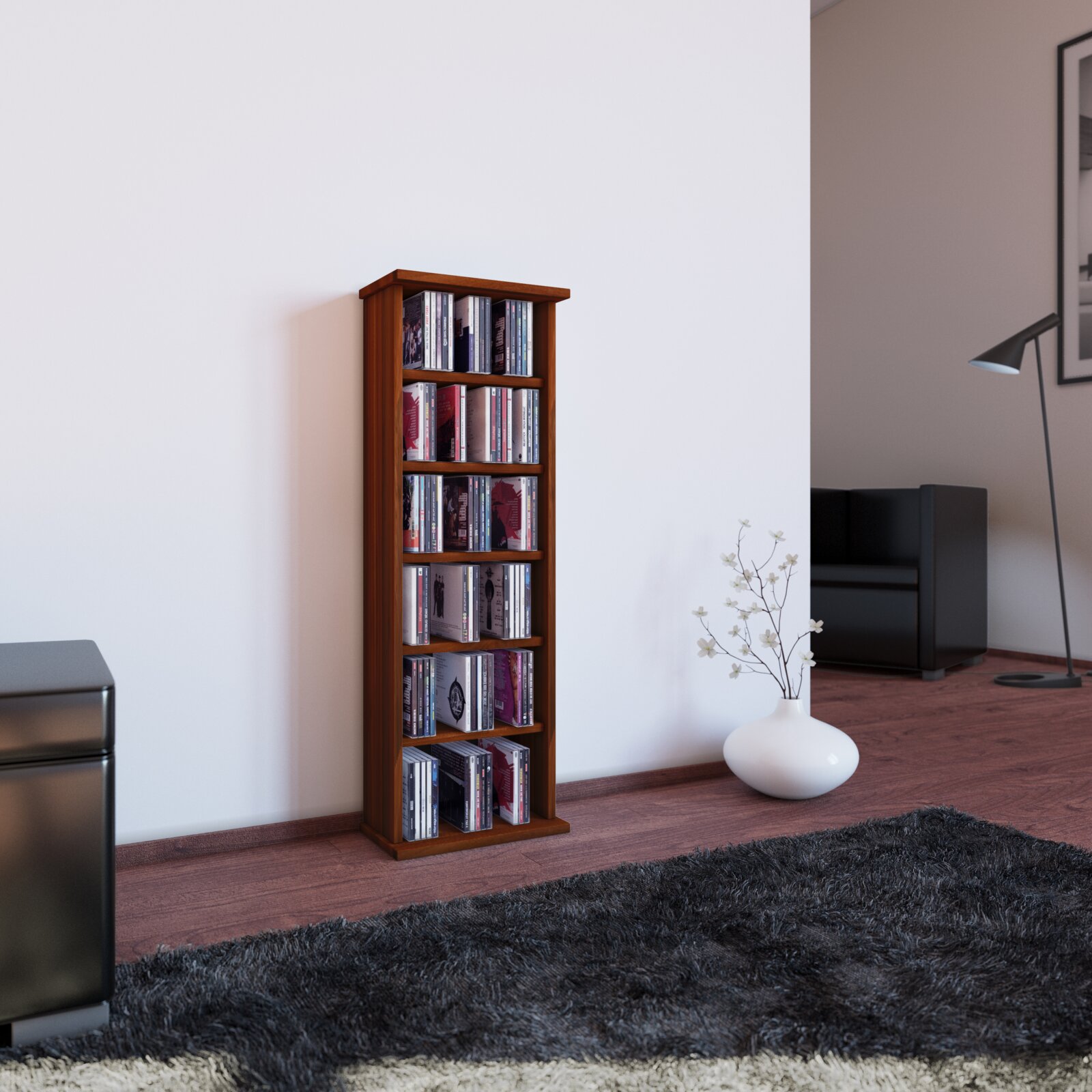 Schmales, hohes CD-Regal aus dunklem Holz mit mehreren Fächern, gefüllt mit CDs, im Wohnzimmer vor weißer Wand perspektivische Ansicht leicht von vorn links.