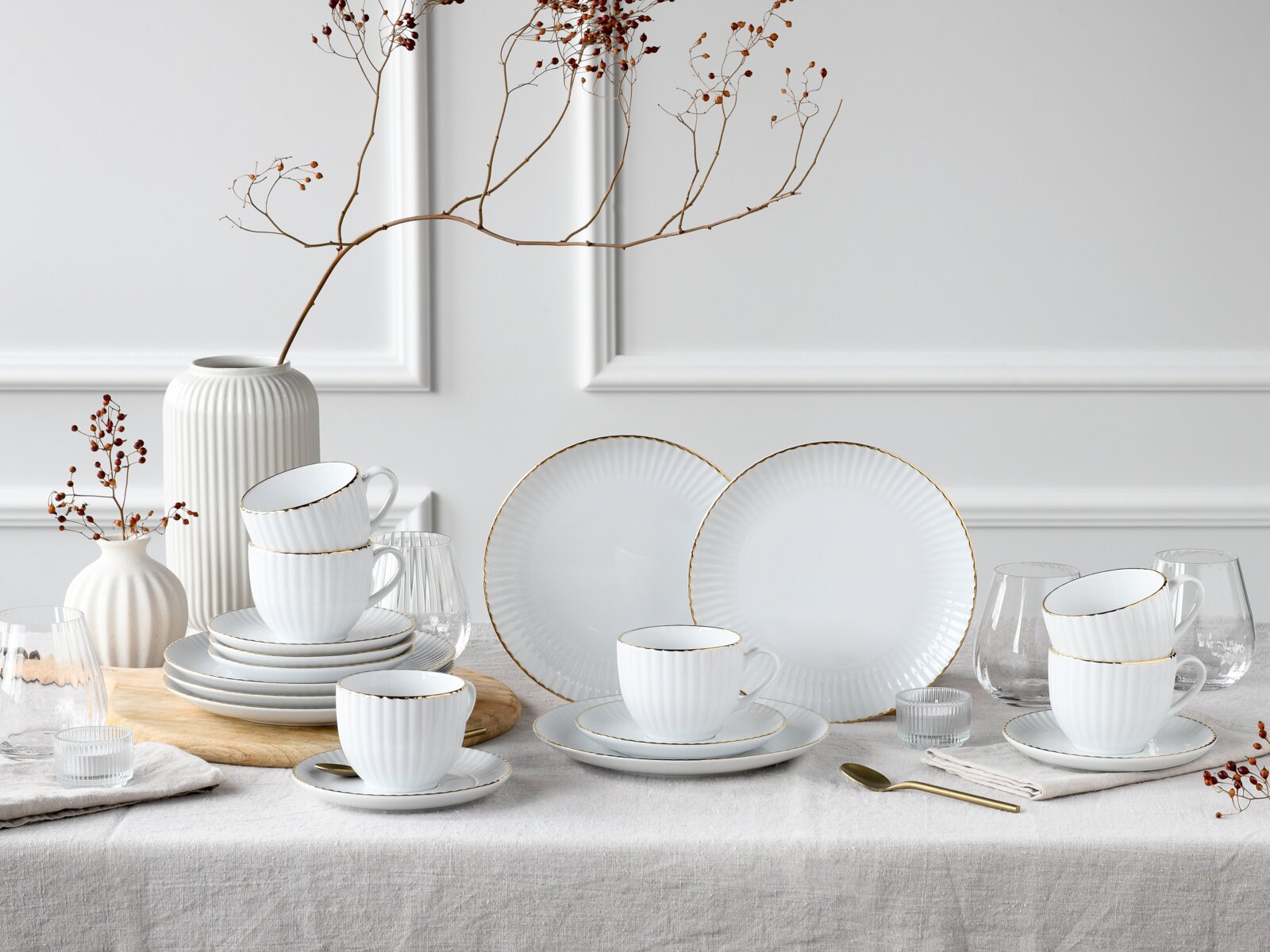 creaTable Kaffeeservice 18-tlg ALLEGRA Schlichtes weißes, geriffeltes Porzellan-Geschirrset mit goldfarbenem Rand (Tassen, Untertassen und Teller) dekorativ auf einem gedeckten Tisch arrangiert, Frontansicht leicht schräg von oben.