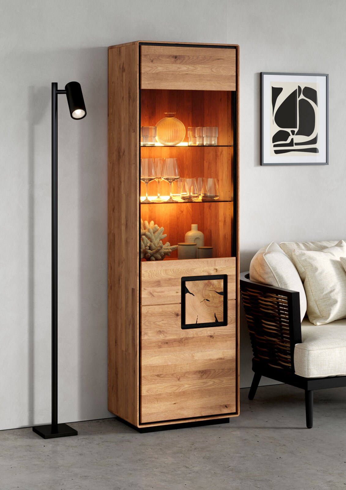 Landscape Vitrine I (links) BRIXEN Hohe, schmale Holz-Vitrine im modernen Design mit warm beleuchtetem Glasfach und geschlossener Front, in einem Wohnzimmer neben Sofa und Stehlampe, perspektivisch frontal mit leichter Linksansicht aufgenommen