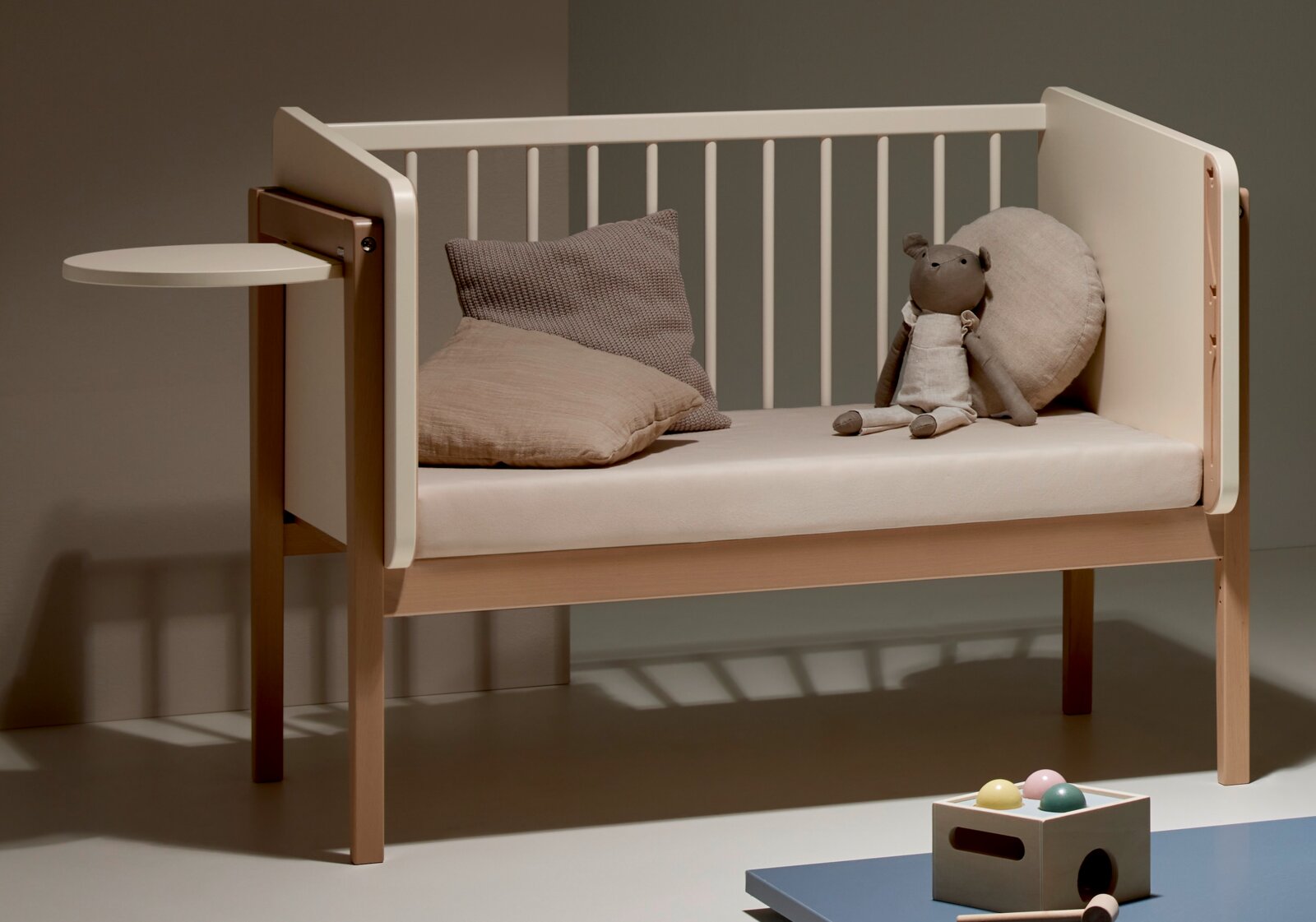 Kinderbett mit seitlichem Tischchen, Kissen und Stofftier, seitliche Perspektive