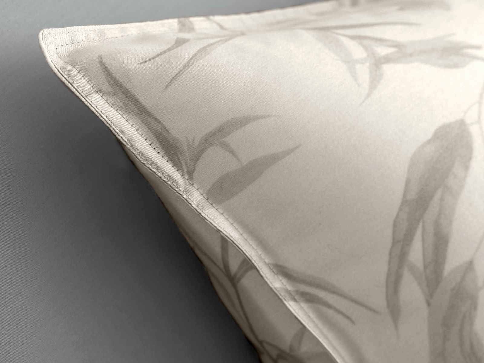 Nahaufnahme einer Bettwäsche mit dezentem Blattmuster in Grau auf hellem Hintergrund, perspektivisch von der Seite aufgenommen.