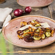 Nahaufnahme eines Tellers aus dem Geschirrset Terra mit einem Gericht aus Gnocchi, Pilzen, roten Zwiebeln und Käsescheiben, auf einem rustikalen Holztisch serviert.