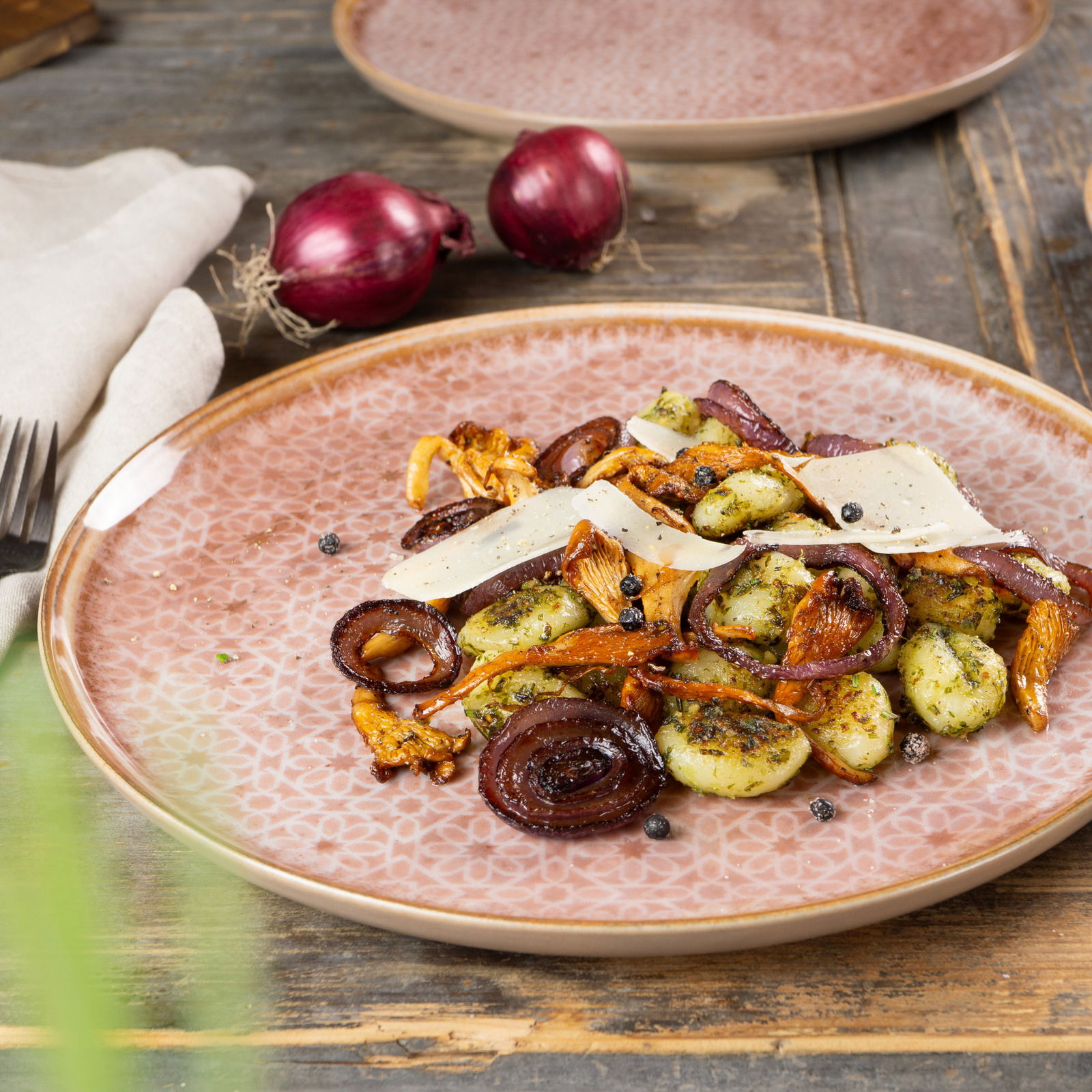 Nahaufnahme eines Tellers aus dem Geschirrset Terra mit einem Gericht aus Gnocchi, Pilzen, roten Zwiebeln und Käsescheiben, auf einem rustikalen Holztisch serviert.