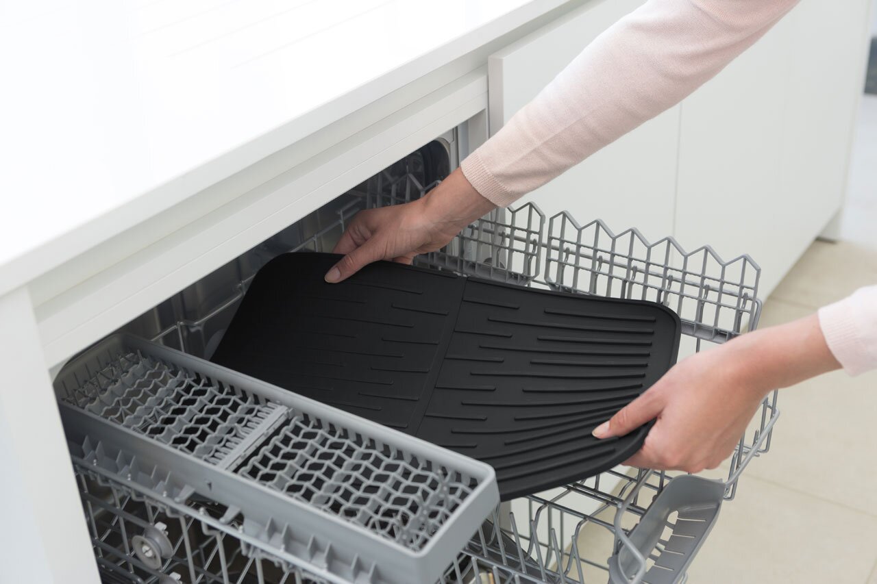 Schwarze Abtropfmatte wird in eine Spülmaschine gelegt, Ansicht von oben.