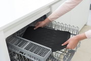 Schwarze Abtropfmatte wird in eine Spülmaschine gelegt, Ansicht von oben.