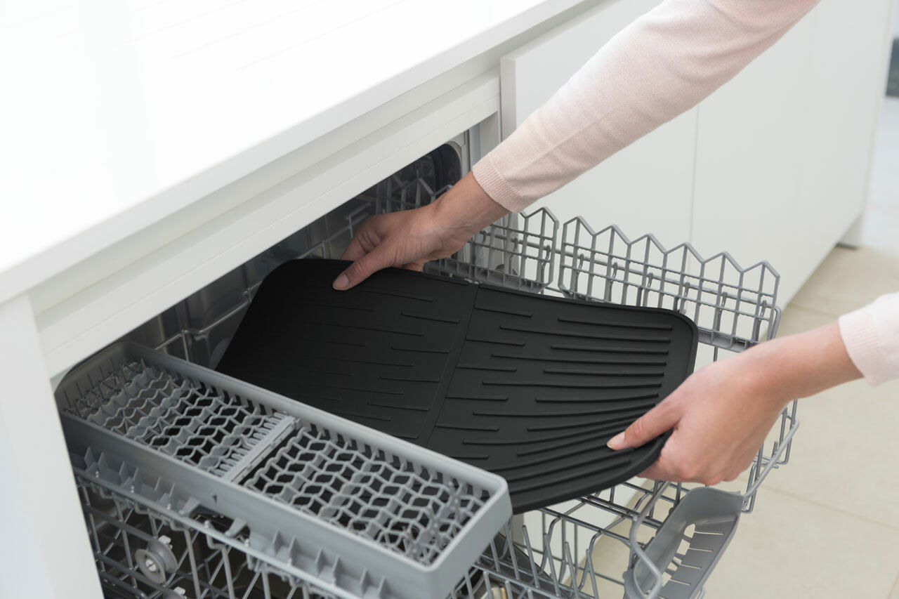Schwarze Abtropfmatte wird in eine Spülmaschine gelegt, Ansicht von oben.
