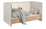 Modernes Kinderbett in Weiß und Naturholz mit Gitterseite, bezogen mit Bettwäsche und Kuscheltieren, freigestellt vor weißem Hintergrund, schräg von vorne links fotografiert.