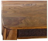 Nahaufnahme einer Ecke eines Esstisches aus Holz mit dekorativen Schnitzereien an der Seite, Perspektive von oben.