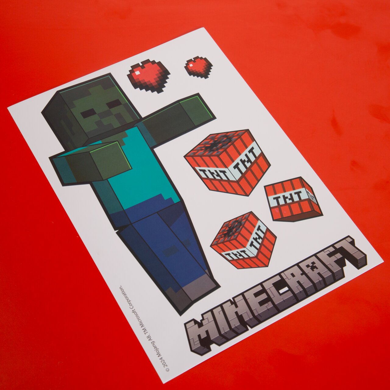 Schräg von oben fotografiertes Minecraft-Bastelvorlagenblatt mit Zombie-Figur, TNT-Blöcken und Pixelherzen auf rotem Hintergrund