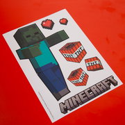 Schräg von oben fotografiertes Minecraft-Bastelvorlagenblatt mit Zombie-Figur, TNT-Blöcken und Pixelherzen auf rotem Hintergrund