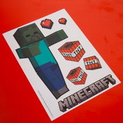 Schräg von oben fotografiertes Minecraft-Bastelvorlagenblatt mit Zombie-Figur, TNT-Blöcken und Pixelherzen auf rotem Hintergrund