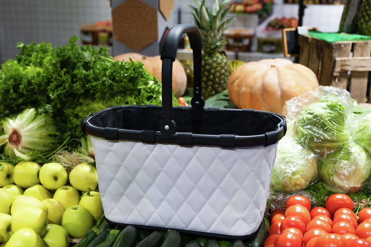 Einkaufskorb mit rhombenförmigem Muster, umgeben von frischem Obst und Gemüse, seitliche Perspektive