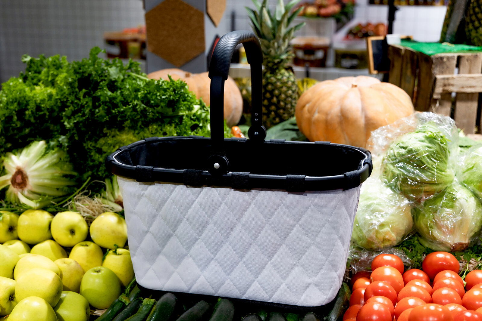 Einkaufskorb mit rhombenförmigem Muster, umgeben von frischem Obst und Gemüse, seitliche Perspektive