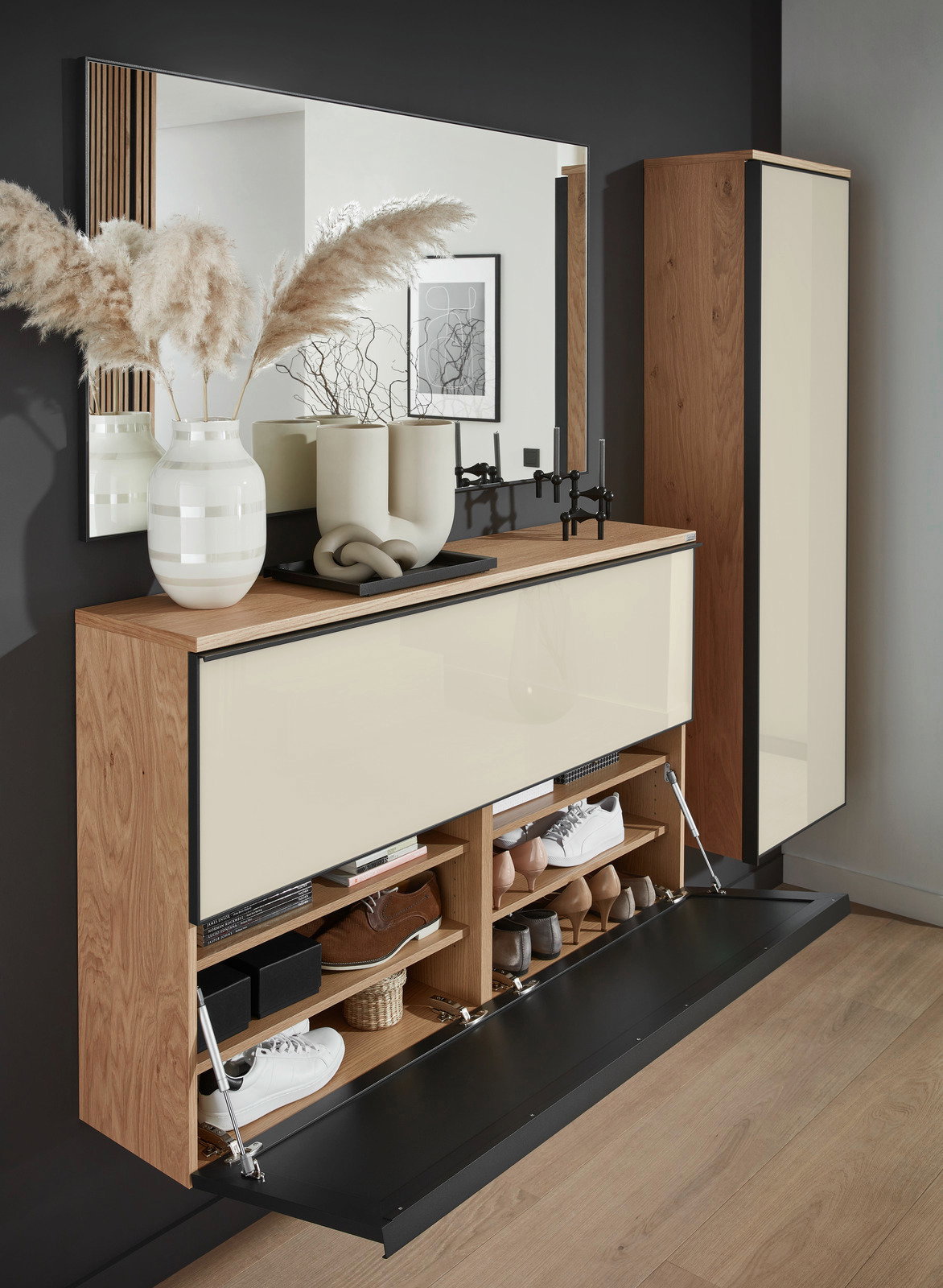 Dieter Knoll Garderoben-Set 5-tlg. ATINA Moderner XL-Hängeschuhschrank aus Holz mit cremefarbenen Fronten, geöffnet, gefüllt mit Schuhen und dekorativen Elementen auf der Oberseite, seitliche Perspektive.