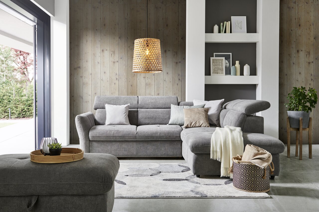 Gemütliche graue Polsterrundecke mit Kissen und Decke, im modernen Wohnzimmer mit Holzvertäfelung und dekorativen Elementen, aus der Frontalperspektive.