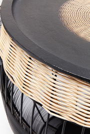 Nahaufnahme eines Beistelltischs mit schwarzer Tischplatte und geflochtenem Rattangestell, seitliche Perspektive.