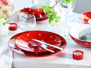 Schwarz-weiß gepunktetes, rotes Keramikgeschirr-Set (Teller, Schale und Tasse) auf weiß gedecktem Tisch mit Besteck und Gläsern, fotografiert in schräger Draufsicht von vorn.